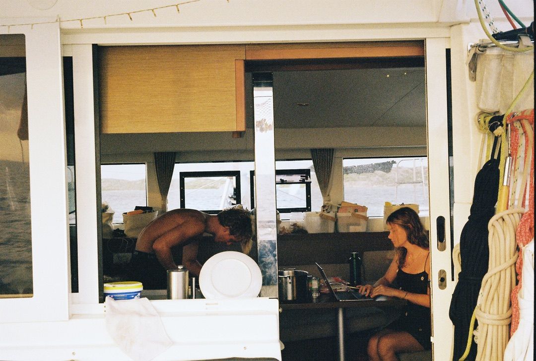 Crew in the galley, one cooking and one working on a laptop