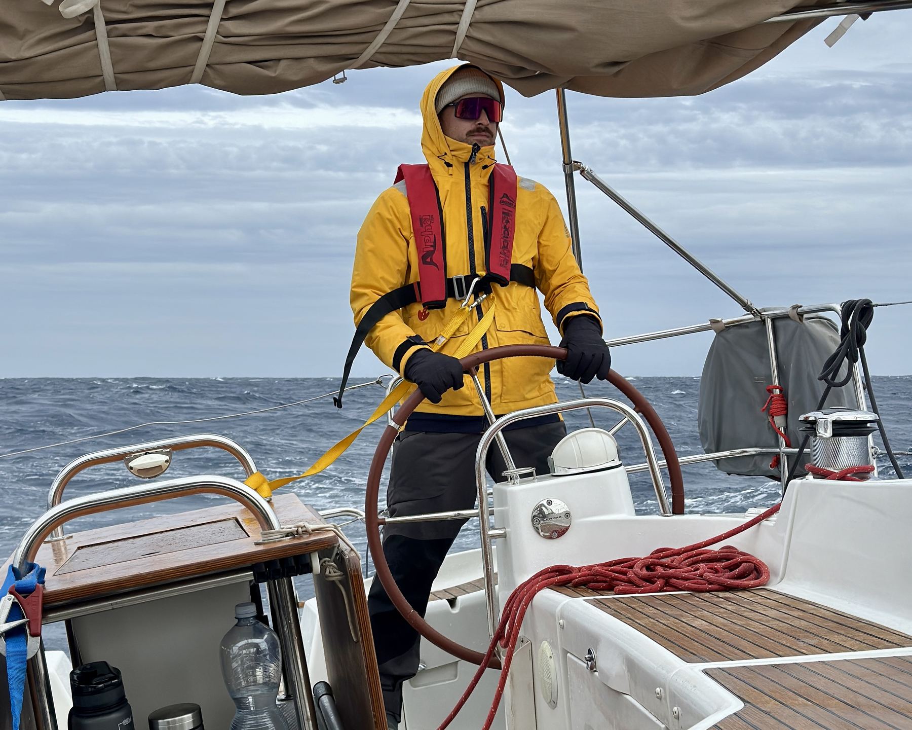 Felix at the helm in foul weather gear during a rough offshore passage